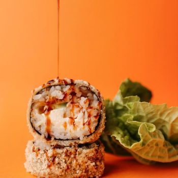a piece of sushi with a lot of sauce against an orange background