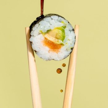 a piece of sushi being held by chopstick with sauce being poured on it