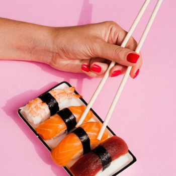 hand picking sushi from a tray of sushi with chopsticks