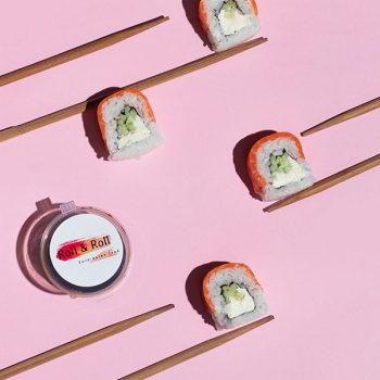 sushi rolls with salmon laid with chop sticks with a pink background